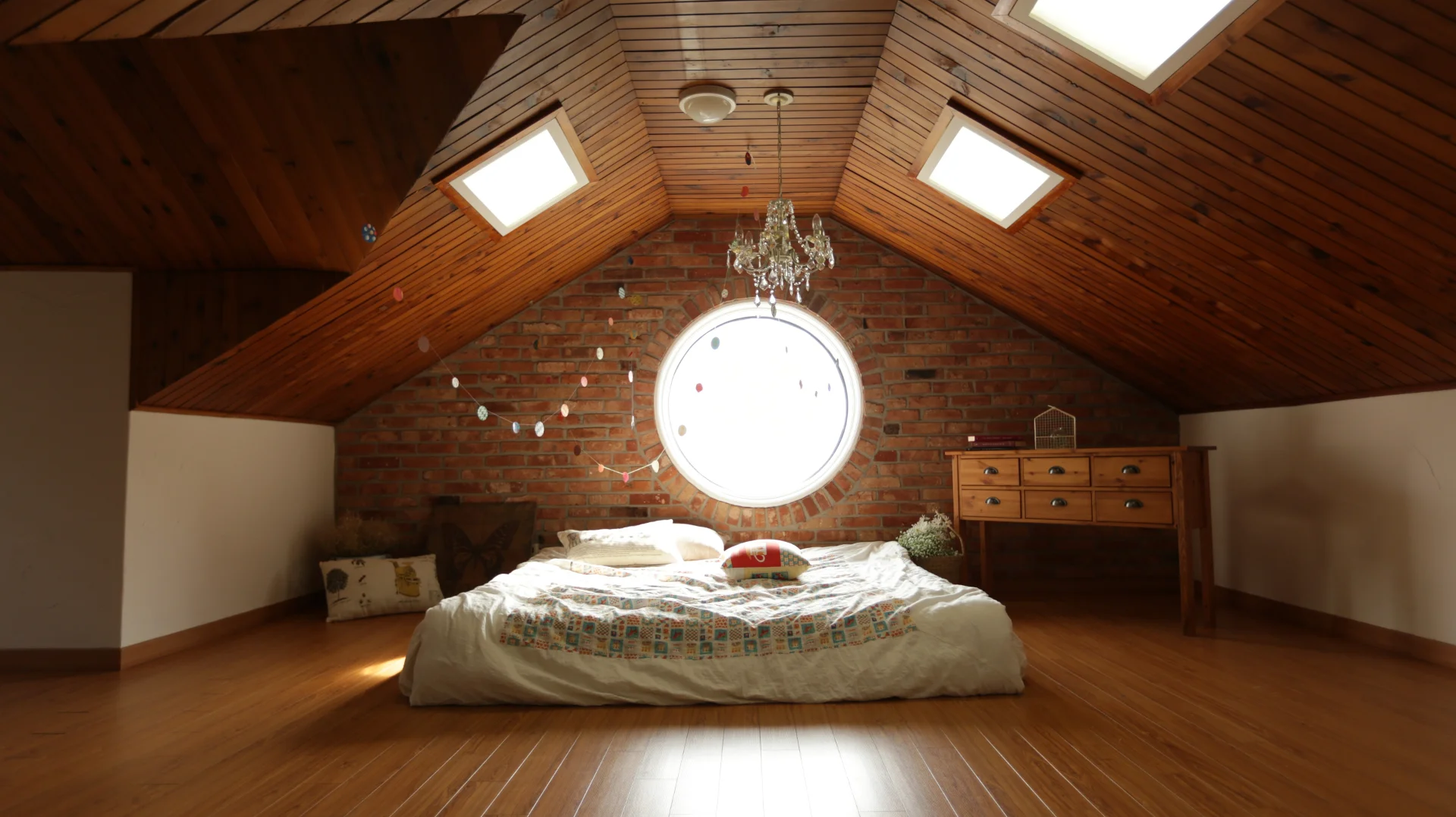 Dans une pièce mansardée avec de belles poutres apparentes, un lit au centre éclairé par une fenêtre sur le mur derrière lui. Ambiance très chaleureuse. Cette photo n’est pas contractuelle et n’est là que pour illustrer le standing de chambre visé.