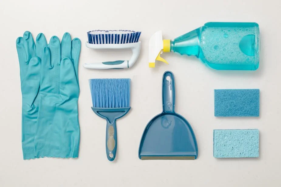 Photo de produit ménager : une paire de gants bleu, une brosse bleu, une balayette bleu, une pelle bleu, une éponge bleu, un gratoire bleu, un spray bleu, l’ensemble sur un fond gris.